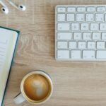 coffee latte near white wireless keyboard and Apple EarPods on the table photography